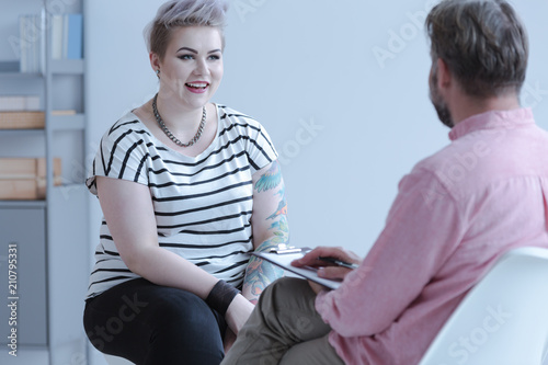 Fototapeta Naklejka Na Ścianę i Meble -  Smiling young woman with tattoos talking with counselor about business