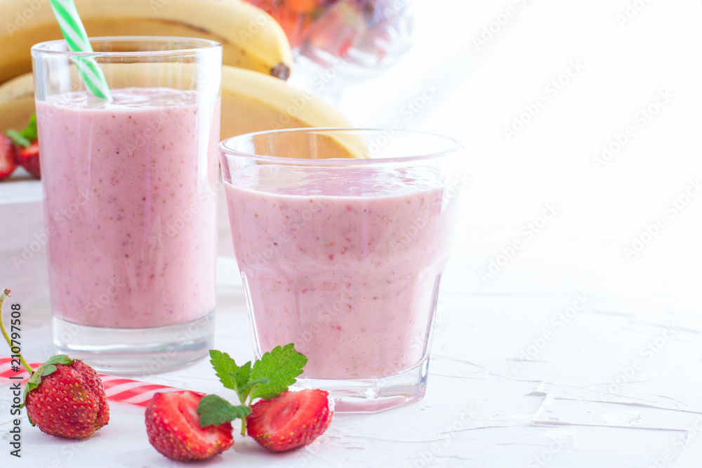 Smoothies of fresh strawberries and bananas in glass glasses on a white table, copy space Smoothies of fresh strawberries and bananas in glass glasses on a white table, copy space