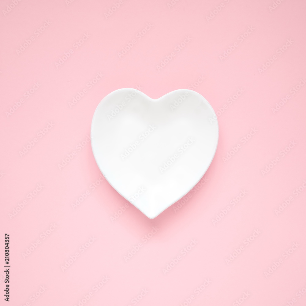 White plate in the shape of heart on a pink background. Flat lay, top view, copy space, square 