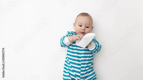 Smiling baby wearing blue striped romper plays with paper boat photo