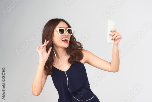 Happy carefree young woman dancing and listening to music from smartphone over grey background