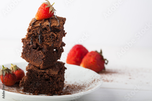 Stack of brownies decorated with strawberries on white plate on white background. Copy space.