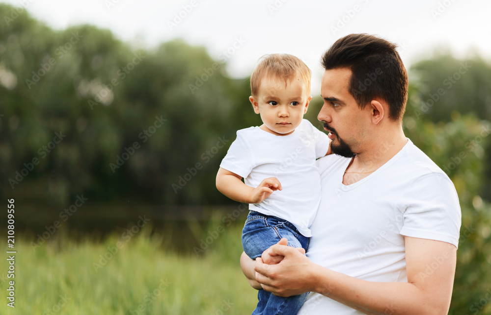 Father tells his son something holding him in arms. Father and son together outdoors. Green background. Happy family concept. Mild colors. Room for copy text Father tells his son something holding him in arms. Father and son together outdoors. Green background. Happy family concept. Mild colors. Room for copy text