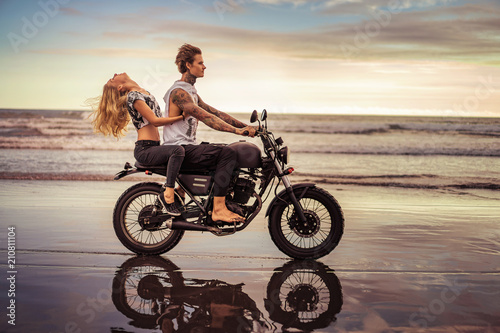 side view of young couple riding motorcycle on ocean beach