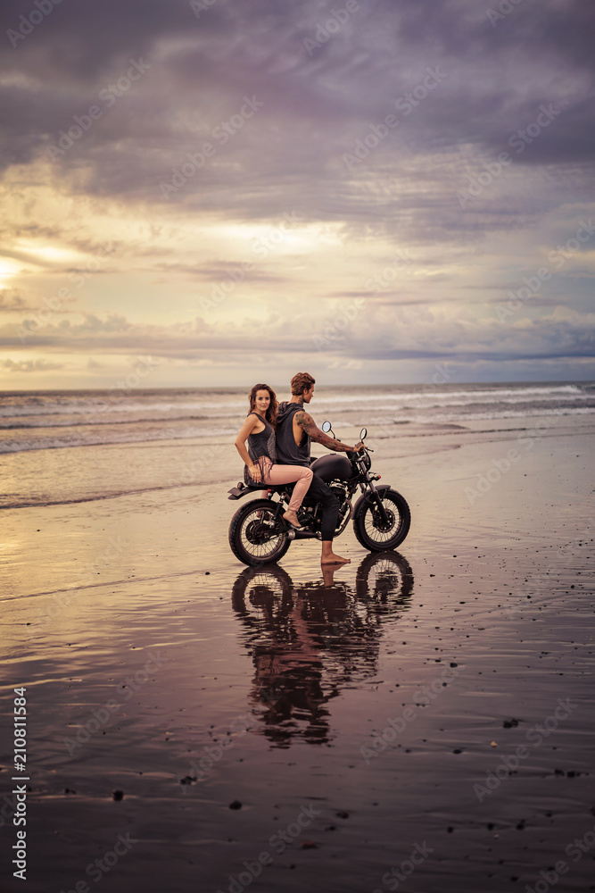 Fototapeta premium boyfriend and girlfriend sitting on motorcycle at beach during sunrise and cloudy weather