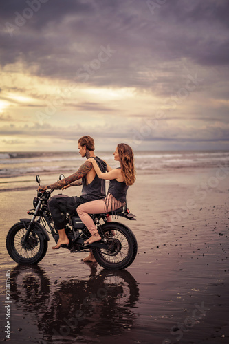 side view of couple sitting on motorcycle at beach during sunrise
