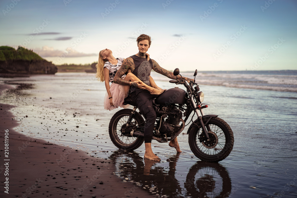 Obraz premium namiętna para przytulanie na motocyklu na plaży oceanu podczas pięknego wschodu słońca