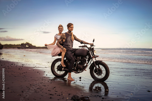 couple sitting on motorcycle on seashore during beautiful sunrise