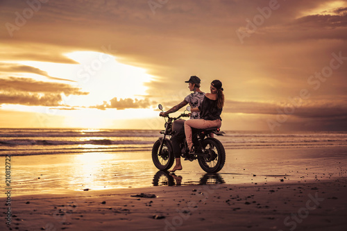 affectionate couple sitting on motorcycle on ocean beach during sunrise