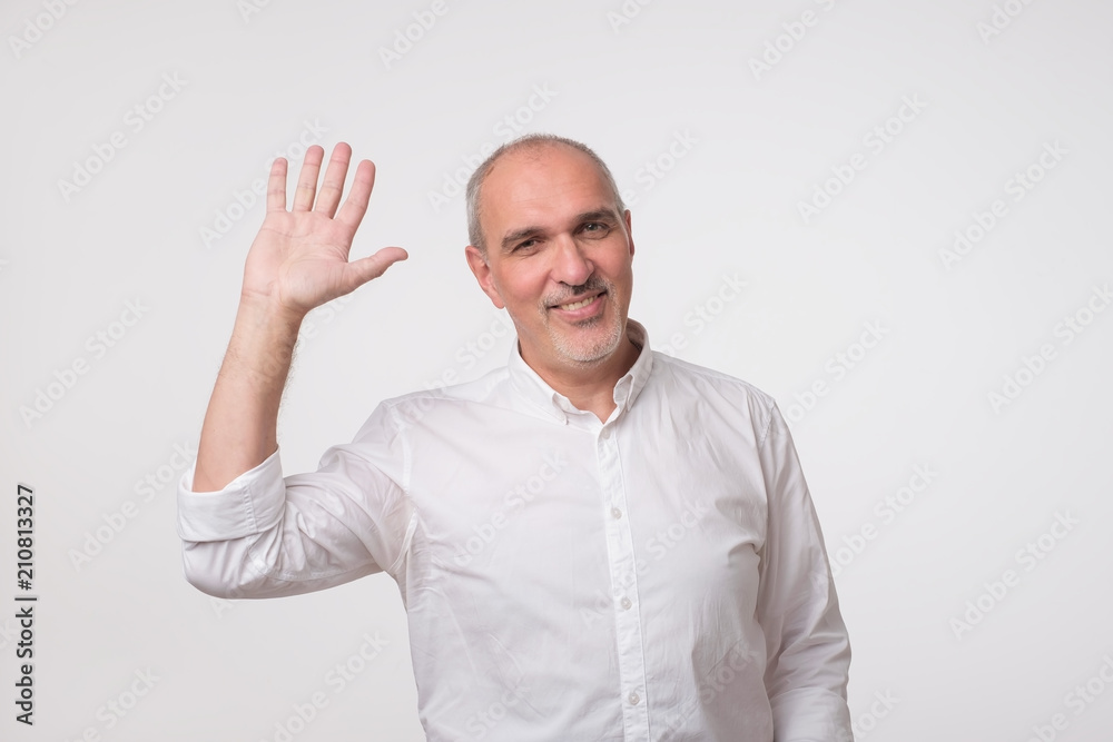 Handsome attractive european man waiving hand in hello gesture while smiling cheerfully.