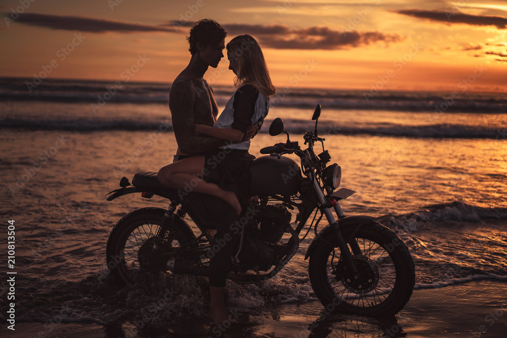 Fototapeta seductive couple hugging on motorbike at beach during sunset