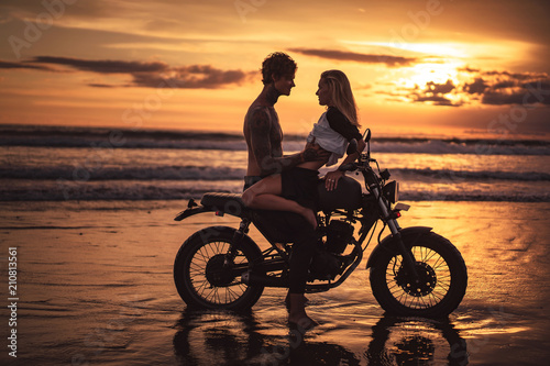 sensual couple hugging on motorbike at beach during sunset