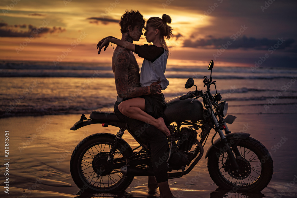 Fototapeta namiętna para przytulanie na motocyklu na plaży podczas zachodu słońca