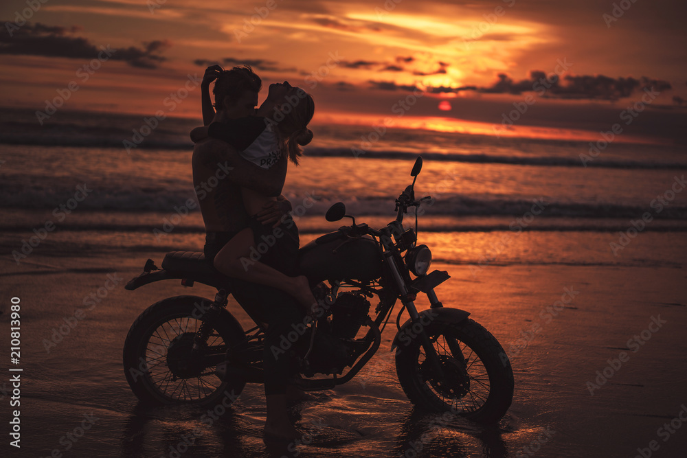 Fototapeta sexy couple hugging on motorcycle at beach during sunset