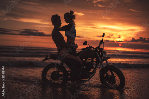 seductive couple hugging on motorcycle at beach during sunset