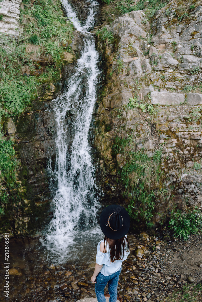 Girl in the hat stands on the background of the waterfall. Enjoying Nature, of concept adventure active vacations outdoor