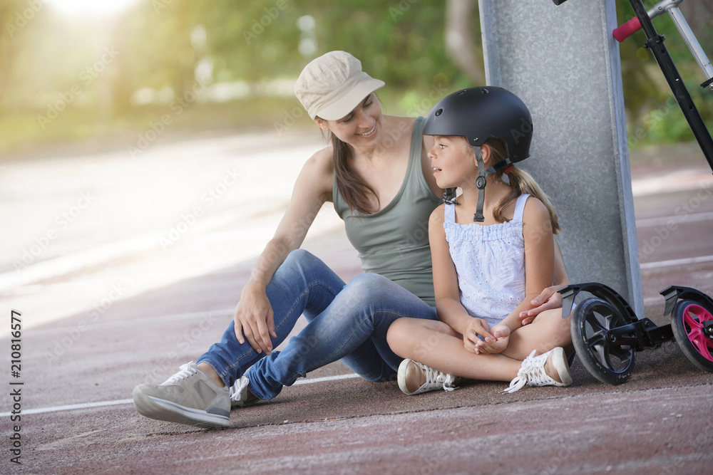 Young girl with mom sitting on floor after riding scooters