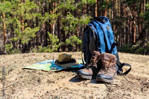 Tourist backpack with hiking boots, hat, compass and map on the glade in pine forest