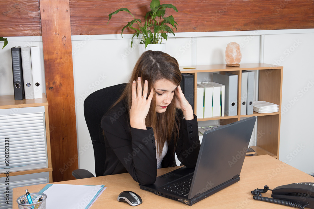 Thoughtful tired businesswoman sitting at desk looking at computer in her office Thoughtful tired businesswoman sitting at desk looking at computer in her office
