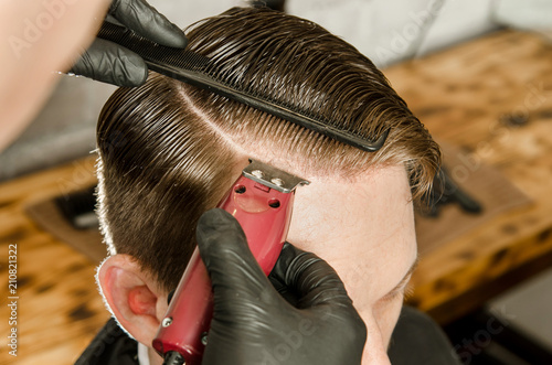 Barber does hair cut and shaves the parting adult man on a brick wall background. Close up.