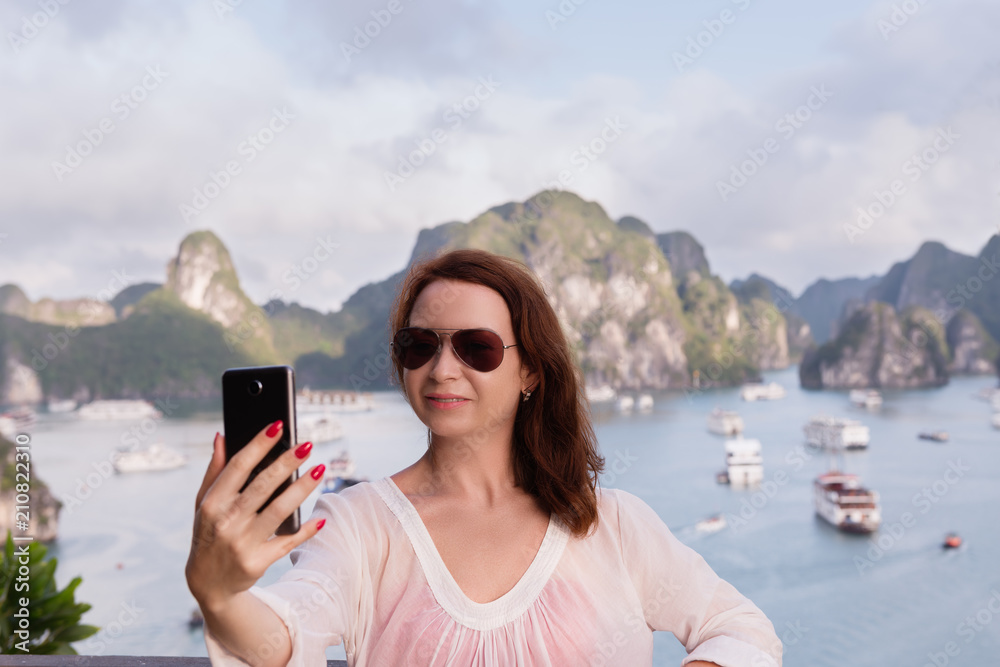 Be online in travel. Modern technology. Young woman doing selfie on the top of hill with sea and islands background