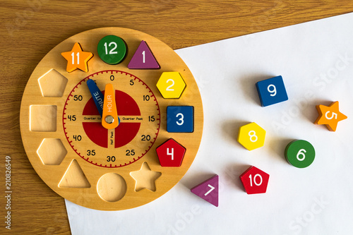 Toy wooden clock on a sheet of white paper, on a wooden background