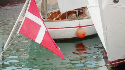 Danish flag waving in front of white boats on a canal with an orange buoy