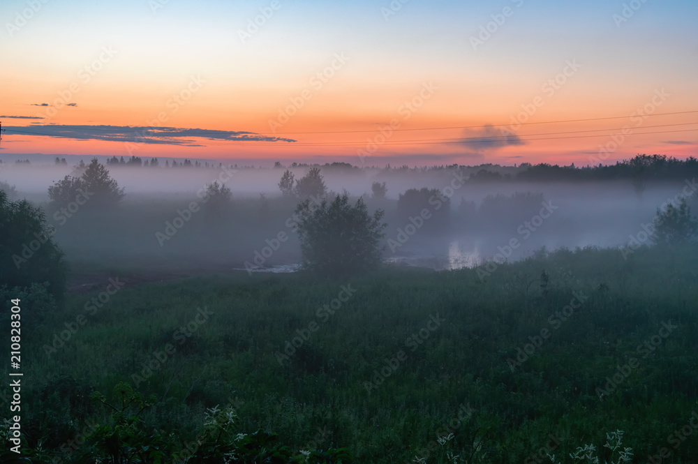 Evening thick fog over field and forest. Landscape of the evening sky with fog, orange and blue sky.