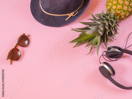 Pineapple, earphones, blue hat and sunglasses on pink background with copy space
