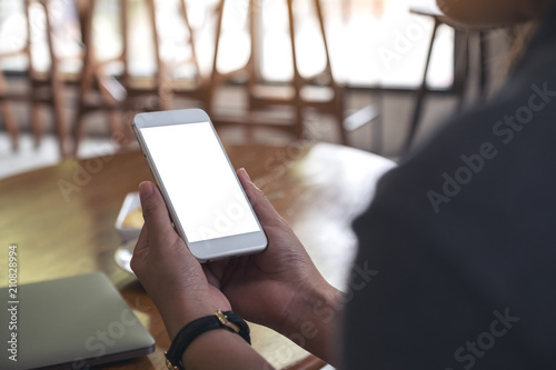 Mockup image of a woman's hands holding white mobile phone with blank desktop screen in cafe