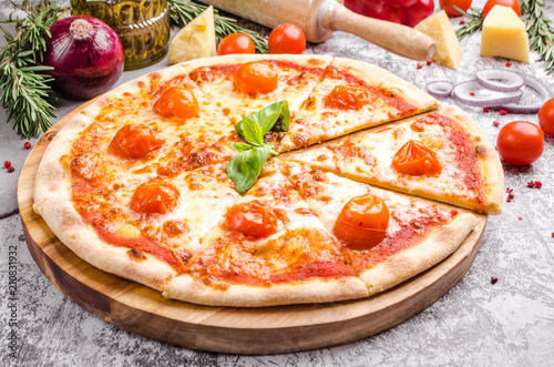 Homemade Meat Loves Pizza with basil, cherry tomatoes, pepperoni sausage, bacon, onions, cucumber, cheese on a wooden board over stone table background, restaurant menu concept. Italian food style
