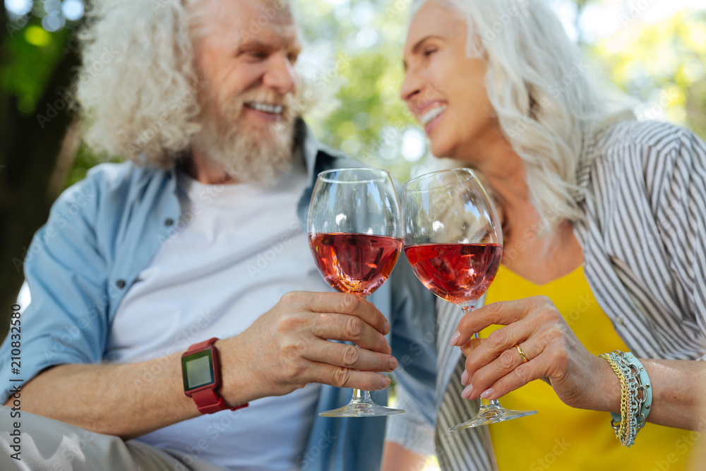 Alcoholic drink. Selective focus of glasses with wine being clinked together by a cheerful elderly couple Alcoholic drink. Selective focus of glasses with wine being clinked together by a cheerful elderly couple