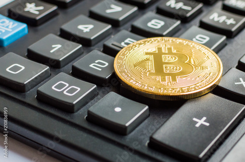 Golden bitcoin coin on calculator close up
