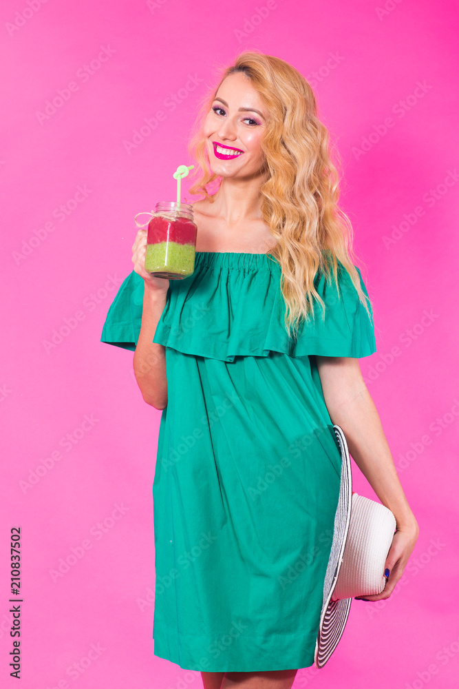 Portrait of young woman holding and drinking tasty green smoothie milkshake on pink background