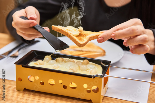 the girl tastes cheese raclette in a cafe. Delicious and with hot steam. swiss food. cheese raclette with mushrooms on coupelles - special small skillet for a raclette