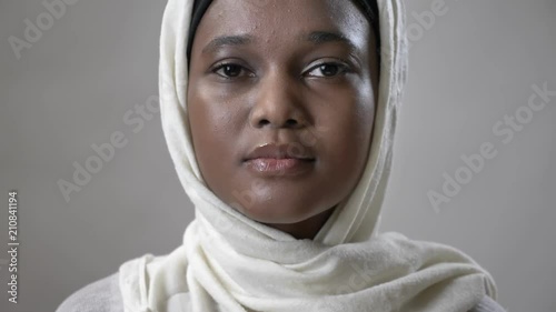 Young sad african muslim girl in hijab is looks up and watching at camera, religioun concept, grey background photo