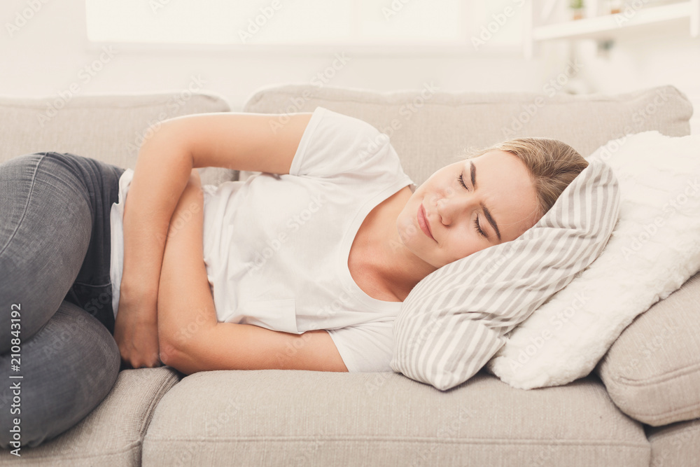 Sad woman with stomach ache on couch at home Sad woman with stomach ache on couch at home