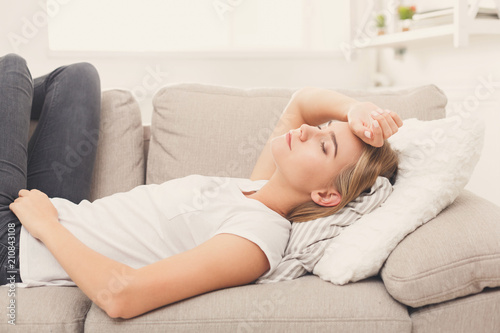 Sad blonde girl feeling pain lying on sofa