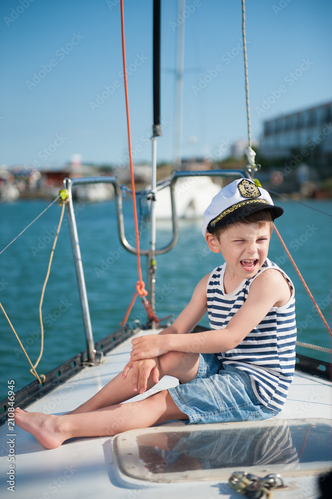 handsome little funny kid in captain hat on sea boat board in summer cruise
