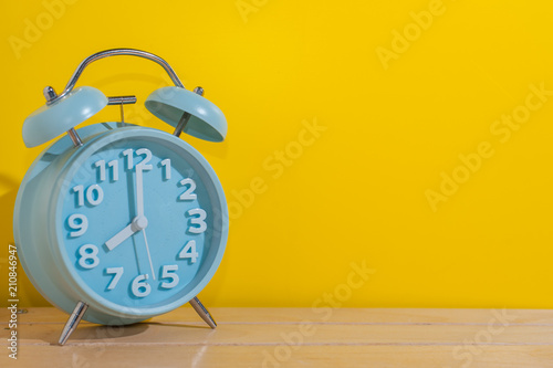 Blue analog alarm clock on wooden table with Yellow Background.