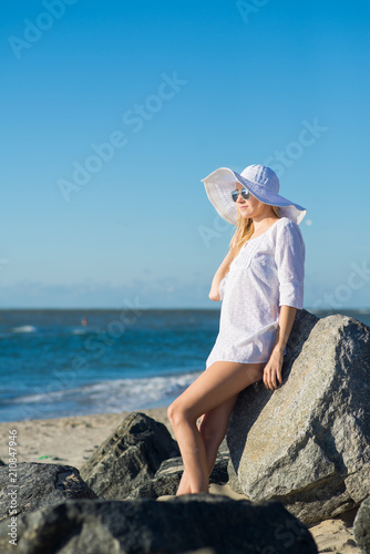 Attractive woman in white dress, big hat and glasses relaxing on the beach on sunny day