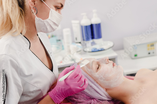 Female cosmetician doctor applying cream on face of young woman