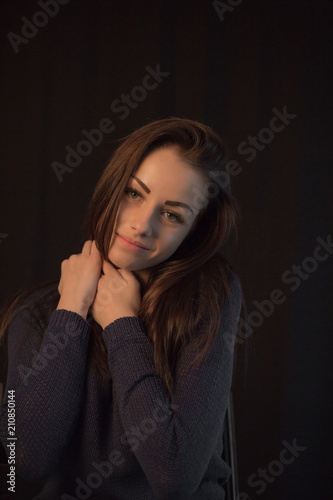 Beautiful young girl wearing sweater posing on black studio background touching her head with hand