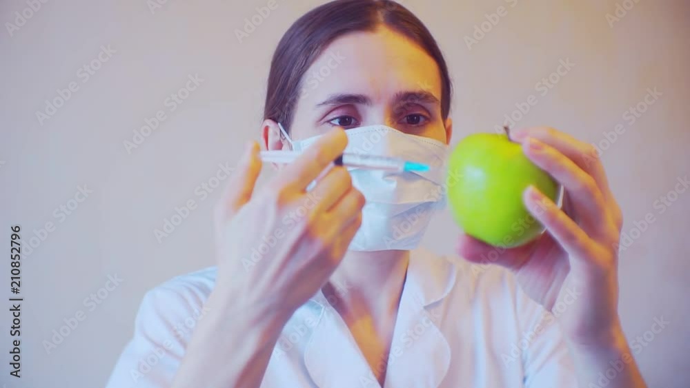 Portrait of a female doctor who makes an injection into ripe apple Portrait of a female doctor who makes an injection into ripe apple
