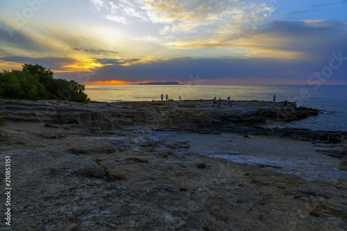 Group of people on edge watching beautiful colorful sunset at the sea with dramatic clouds and sun shining. Beauty world natural outdoors travel background