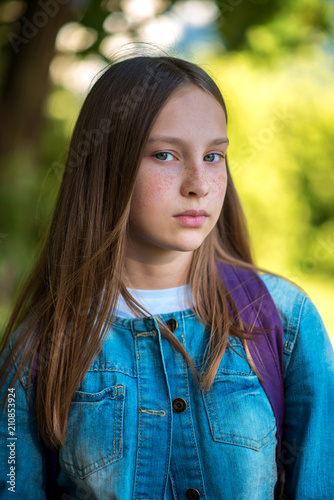 Close-up portrait. Girl schoolgirl. In a denim jacket behind backpack. Long hair freckles on face. Beautiful and intelligent look of the girl.