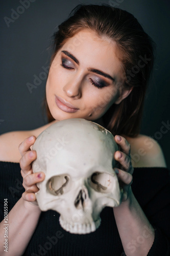 A beautiful girl in black clothes with a skull in her hands. Gothic fashion. A model on a gray background. Studio portrait