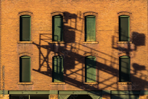 Green window shutters on a red brick building with an interesting shadow and symetry. photo