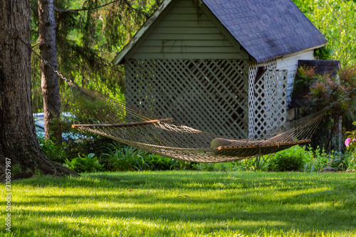 A white hammock in a yard with green grass and little shed.