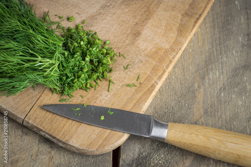 Chopped fresh dill on a cutting Board and a bunch of dill on a wooden table